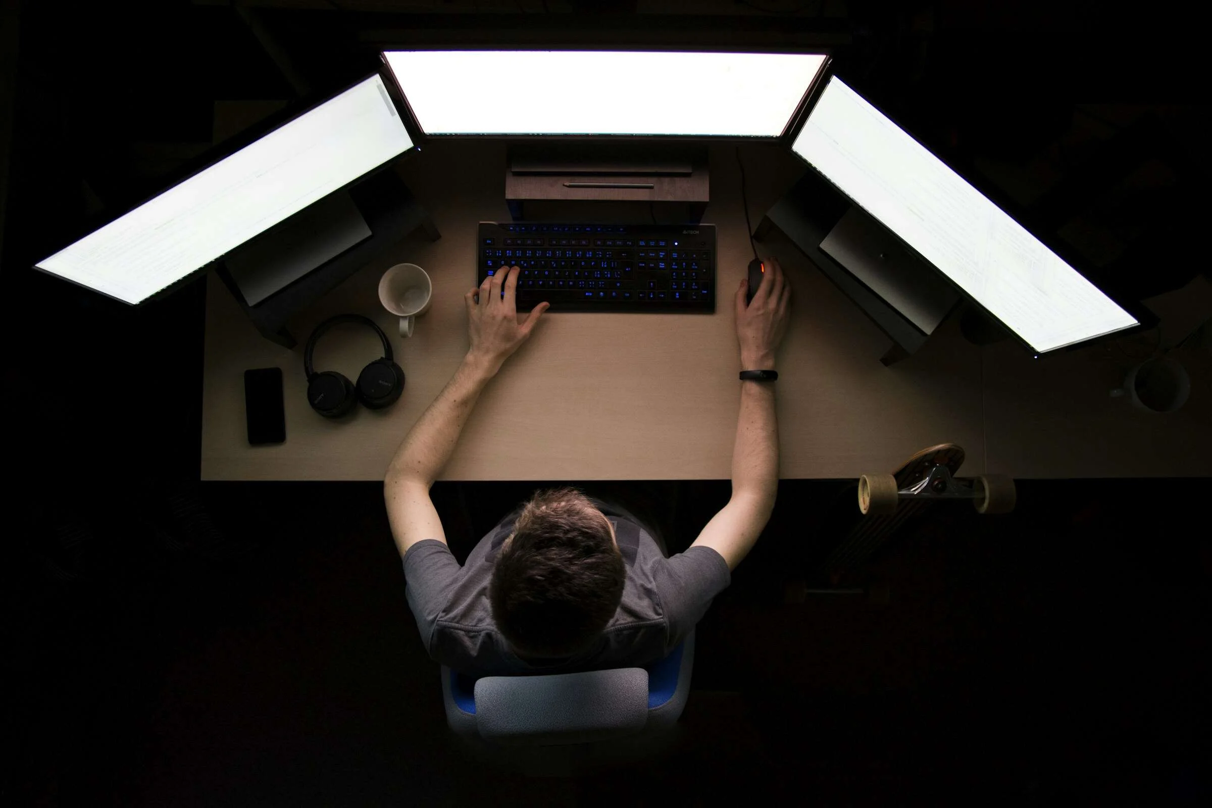 Persona de espaldas programando de noche frente a tres monitores